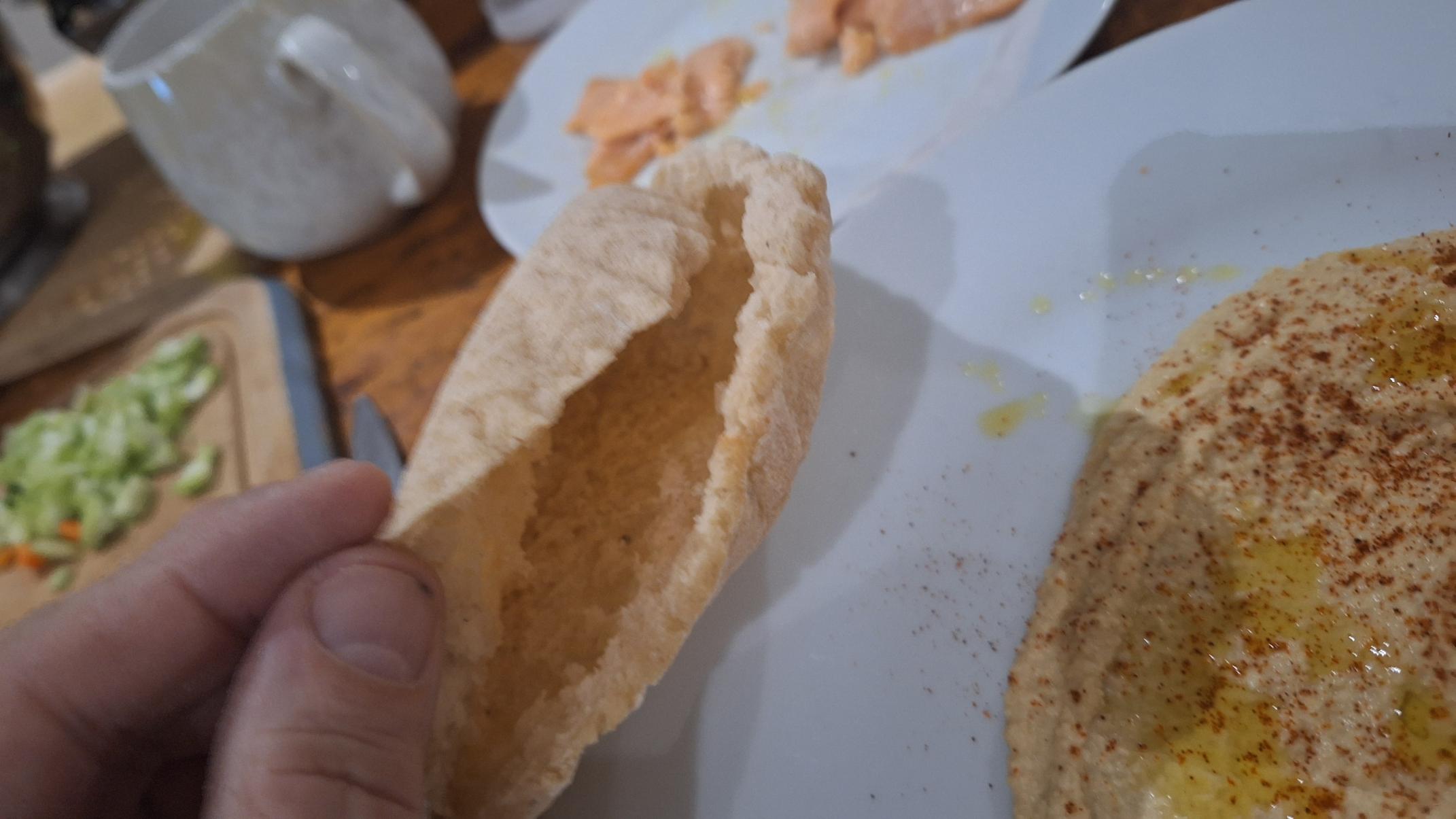 Cut open pita pocket showing interior and plate of home made hummus in background