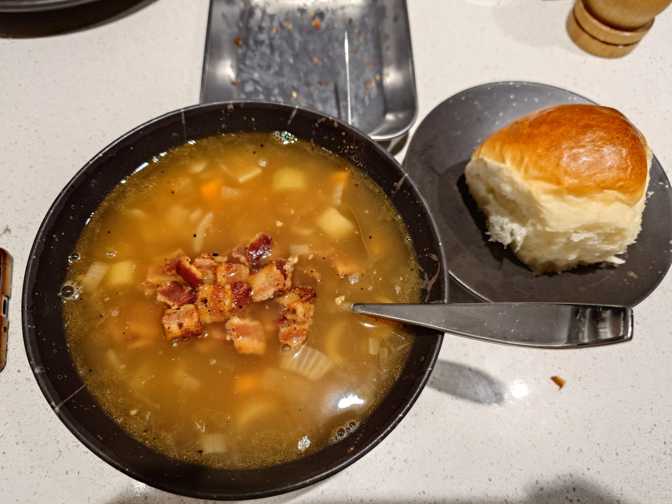 A bowl of soup next to a milk bread roll